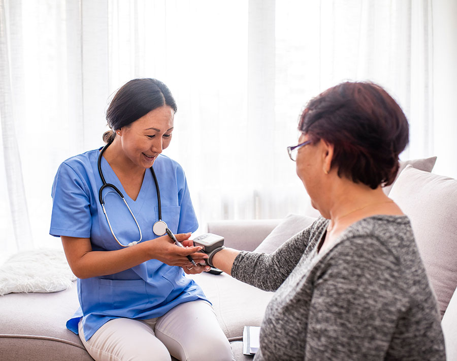 A nurse check a vitals of a women sitting on a couch